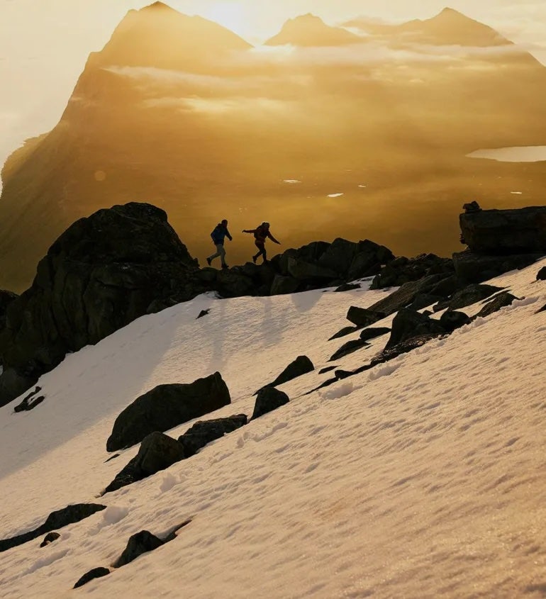 två personer som vandrar på ett snöigt berg i soluppgång